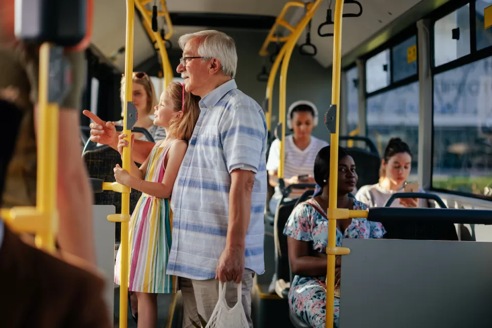 Elderly man and granddaughter standing on public bus.